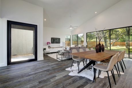 A modern, open-concept living and dining area with wood floors, large windows, and sleek furnishings.