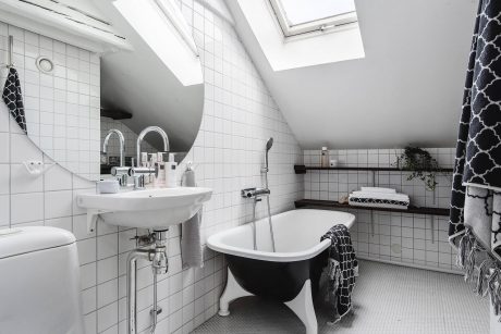 Bright and airy attic bathroom with white tiles, freestanding tub, and skylight.