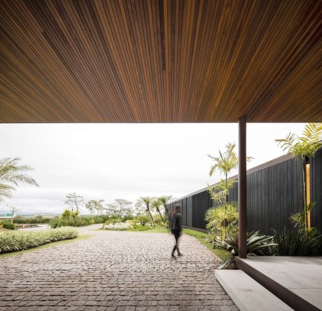 A modern architectural landscape with a wooden canopy, cobblestone path, and lush greenery.