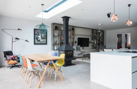 Eclectic open-plan living space with colorful chairs, floating shelves, and a fireplace.