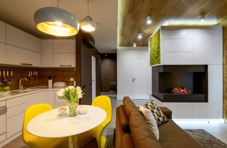 Modern kitchen with sleek cabinetry, pendant lights, cozy living area, and textured fireplace wall.