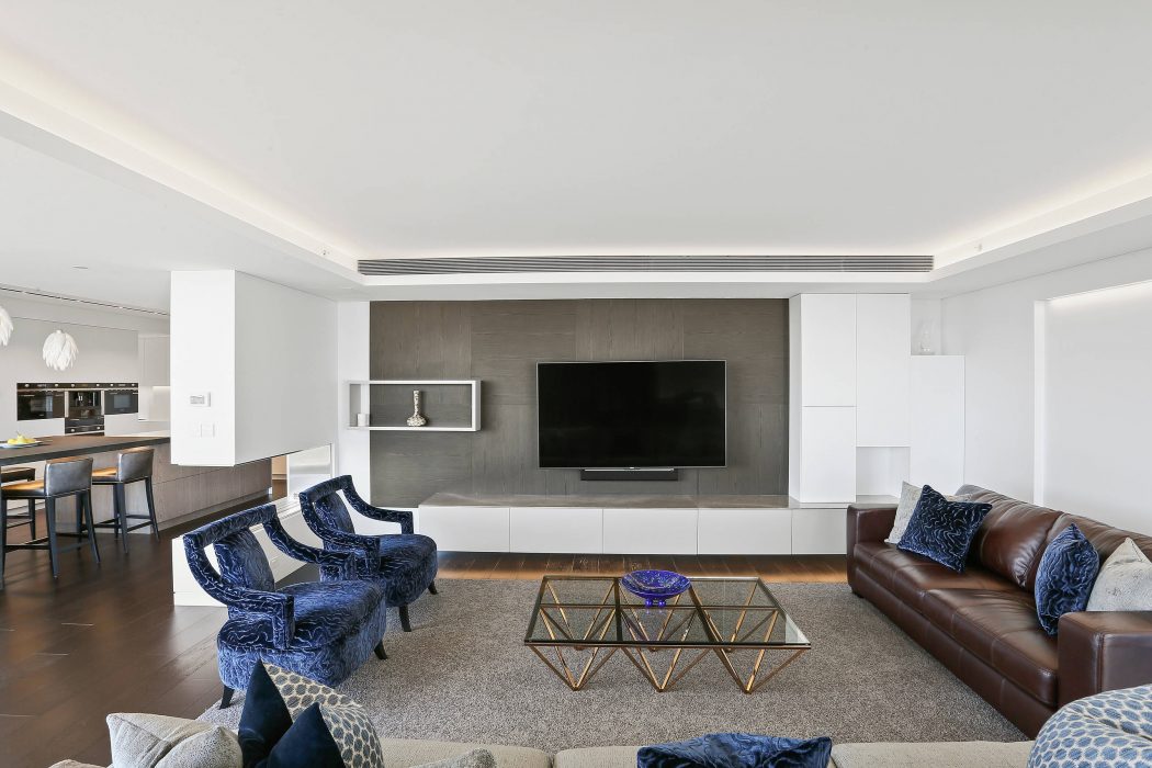 Sleek modern living room with navy blue velvet chairs, leather sofa, and geometric coffee table.