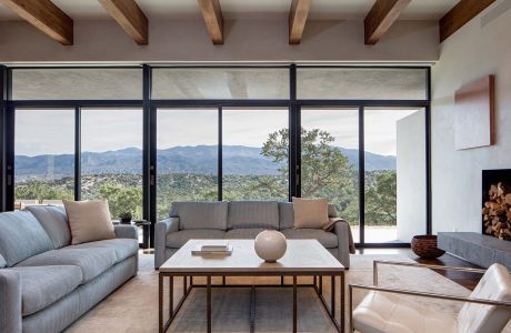 Open floor plan with tall windows showcasing mountain views, wood-beamed ceilings, and neutral-toned furnishings.