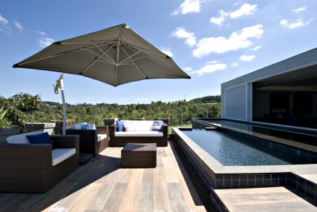Tranquil outdoor pool deck with modern furniture, shade umbrella, and lush greenery.