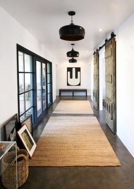 A modern, minimalist hallway with black pendant lights, a wooden bench, and textured flooring.