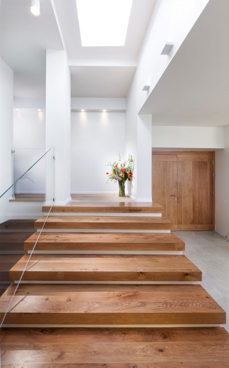 Bright, modern entryway with wooden stairs, glass panel, and a vase of flowers.