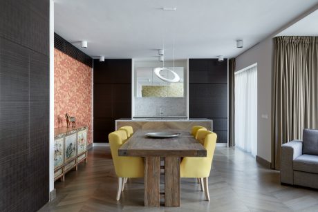 A modern dining area with a rustic wooden table, yellow upholstered chairs, and a patterned cabinet.