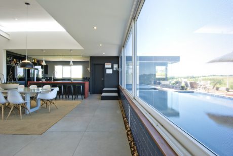 Sleek, modern open-concept kitchen-living space with large glass windows overlooking pool.