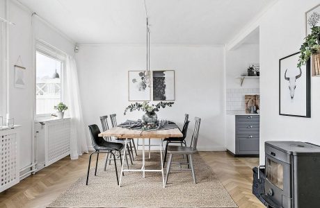 A bright, minimalist dining room with a rustic wood table, black chairs, and art pieces.