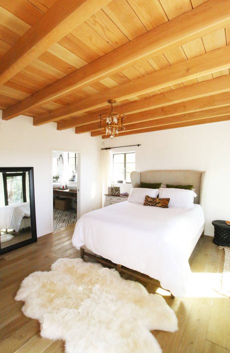 Cozy bedroom with exposed wooden beams, plush rug, and a tasteful chandelier.