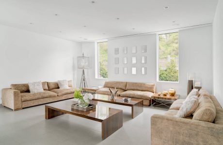 Spacious minimalist living room with large windows, plush sofas, and glass-top coffee tables.