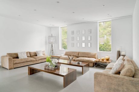 Spacious minimalist living room with large windows, plush sofas, and glass-top coffee tables.
