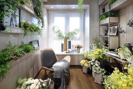 A cozy and lush workspace with a floor-to-ceiling window, built-in shelves, and abundant greenery.