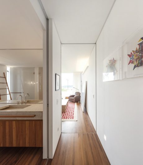 Minimalist hallway with wooden floors, white walls, and a patterned rug leading to a bathroom.
