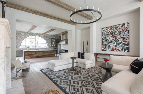 Spacious open-concept living area with stone archway, wood beams, and abstract artwork.