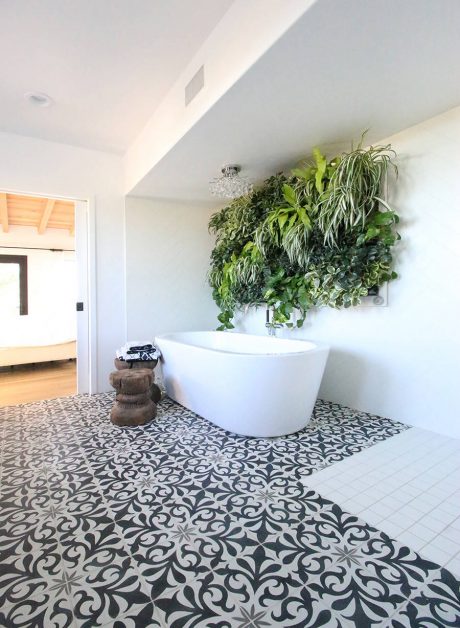 Modern bathroom with lush vertical garden, freestanding tub, and patterned tile floor.