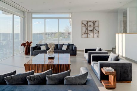 Minimalist living room with floor-to-ceiling windows, dark sofas, and a wooden coffee table.