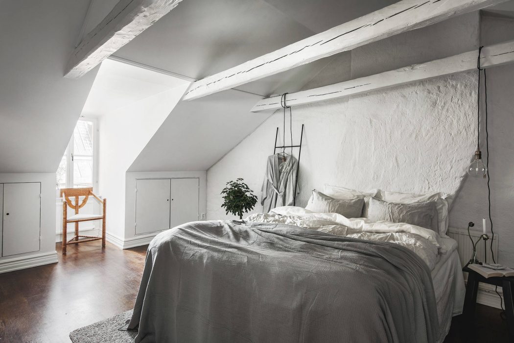 A cozy attic bedroom with white-washed walls, exposed beams, and a plush bedding setup.