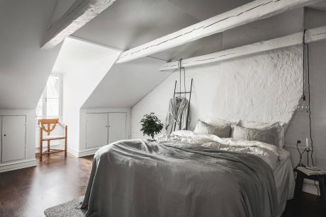 A cozy attic bedroom with white-washed walls, exposed beams, and a plush bedding setup.