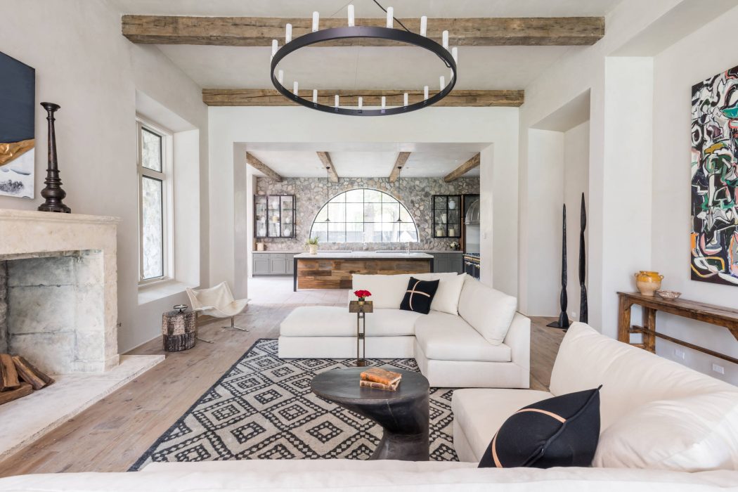 Rustic beams, arched window, modern furnishings, and eclectic artwork in a bright, airy room.