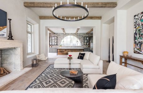 Rustic beams, arched window, modern furnishings, and eclectic artwork in a bright, airy room.