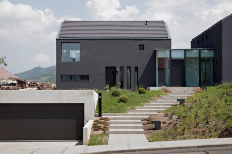 Modern, minimalist home design with sleek grey exterior, large windows, and landscaped steps.