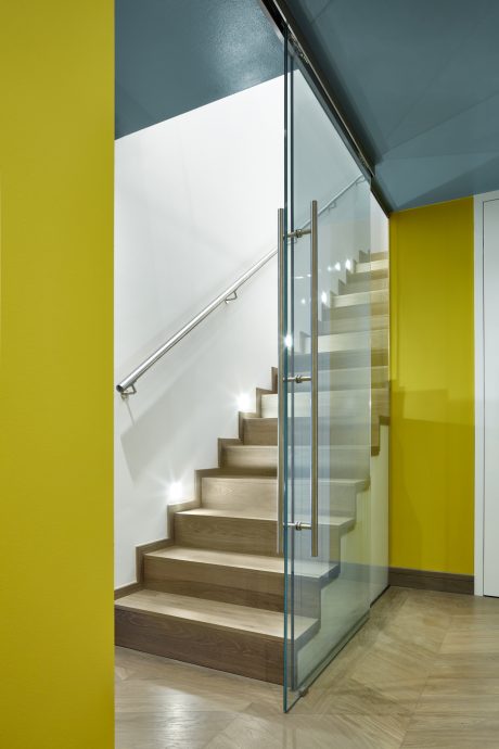 Minimalist staircase with wood treads and glass balustrade, accentuated by vibrant walls.