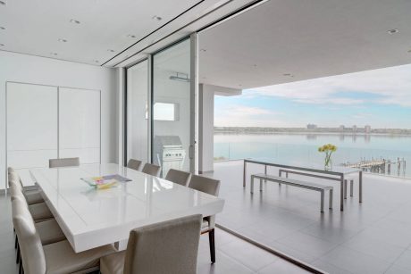 Modern, minimalist dining room with expansive waterfront view and sleek, white furnishings.