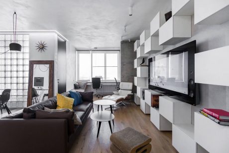 Contemporary open-plan living room with minimalist furniture, shelving, and large windows.