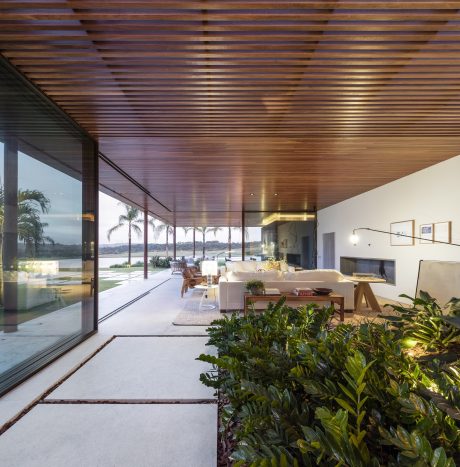 Sleek and modern living space with wood-paneled ceiling, large windows, and lush greenery.