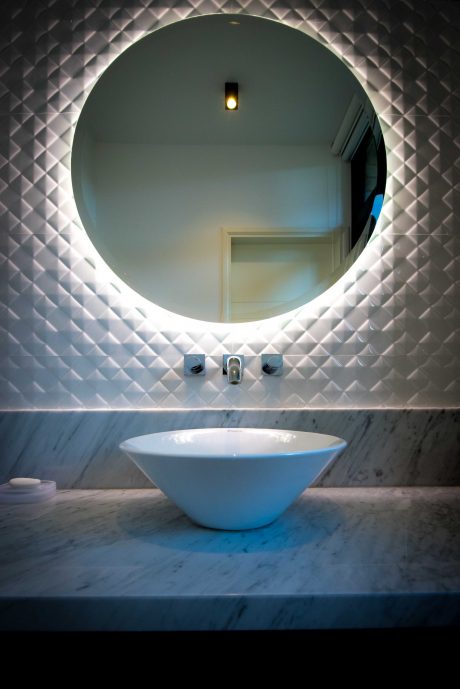 A modern bathroom with a circular mirror, minimalist fixtures, and textured wall tiles.