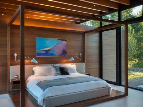 Warm, modern bedroom with wood-beamed ceiling, large windows, and vibrant artwork.