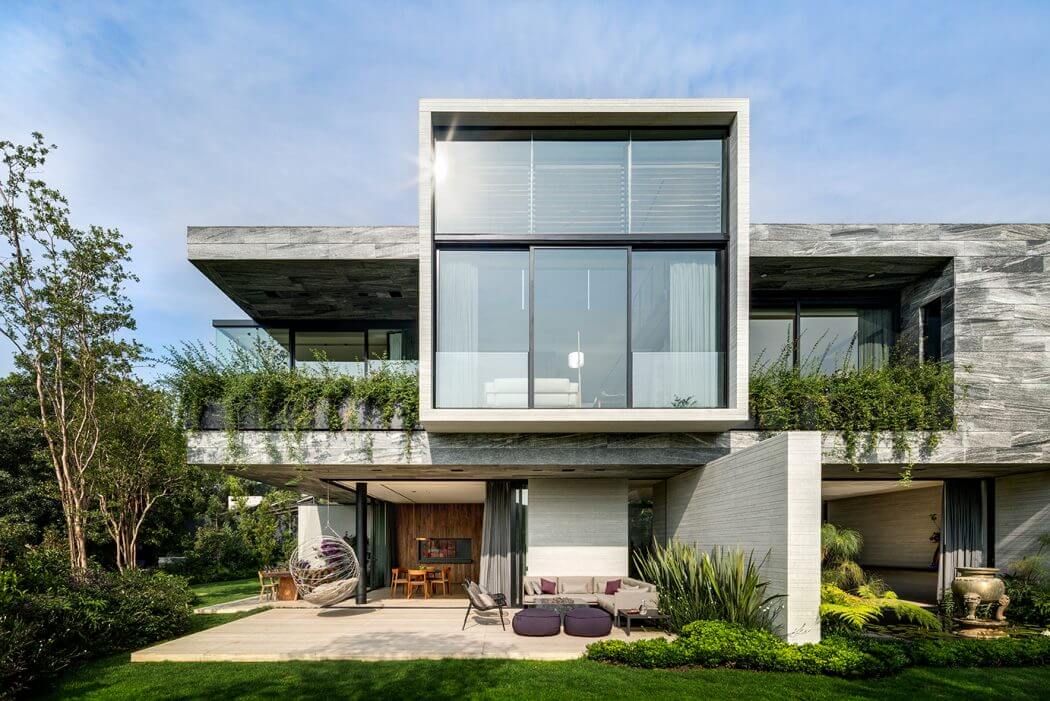 Modern, minimalist house with glass walls, concrete exterior, and lush landscaping.