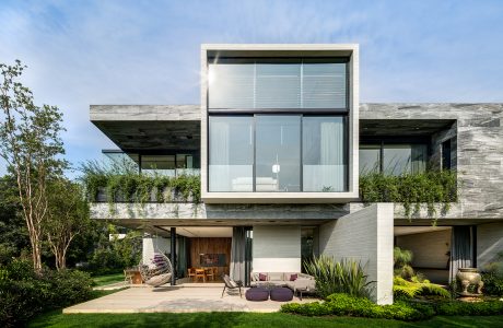 Modern, minimalist house with glass walls, concrete exterior, and lush landscaping.