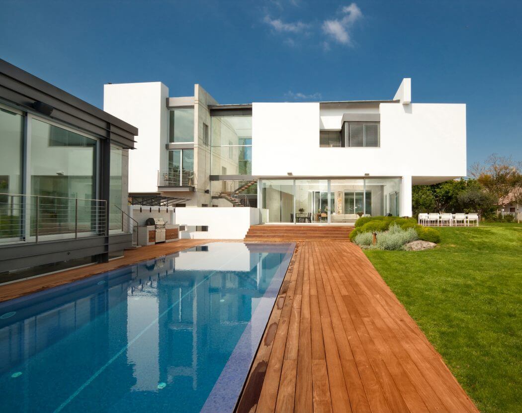 Modern, sleek residential building with a swimming pool, wooden deck, and lush landscaping.
