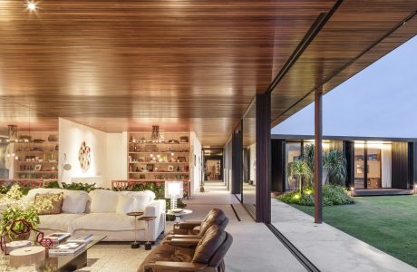 A modern, open-concept living space with a wooden ceiling, large windows, and a view of the outdoor garden.