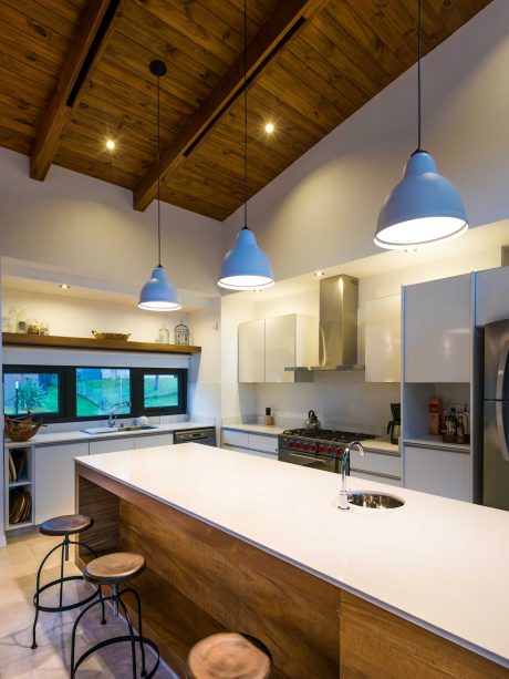 Rustic kitchen with wooden ceiling, blue pendant lights, and minimalist cabinetry.