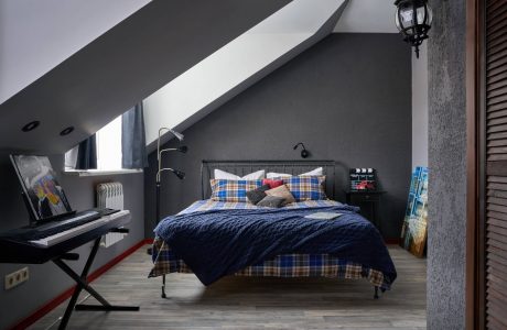 A cozy attic bedroom with sloped ceilings, a plaid bedspread, and a small desk area.