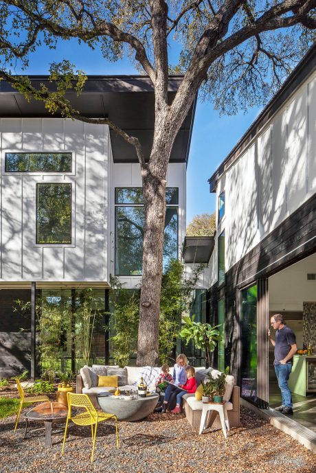 A modern, open-concept home with large windows, a central tree, and a cozy outdoor living space.