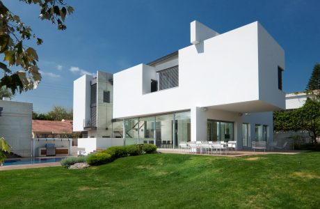 Modern, minimalist architecture with clean lines and large glass windows overlooking a landscaped yard and pool.