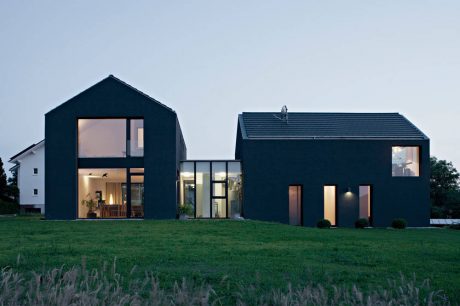 Modern black houses with large windows, surrounded by a grassy field at dusk.