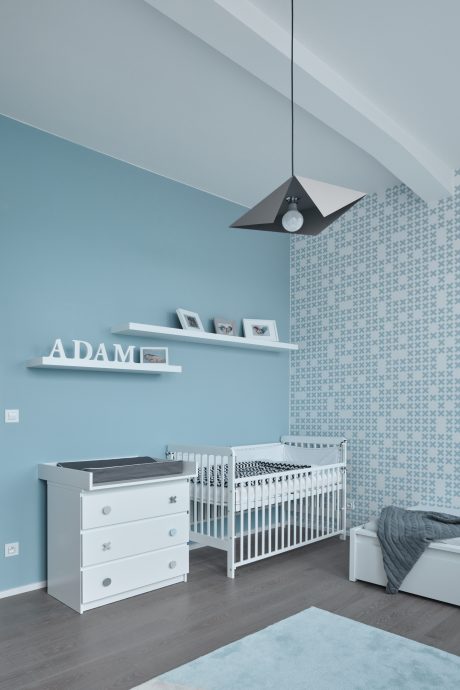 Cozy nursery with modern lighting fixture, patterned wall, and minimalist crib and dresser.