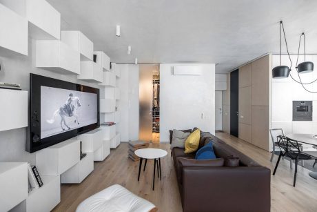 Minimalist living room with wall storage units, large TV, and modern furnishings.