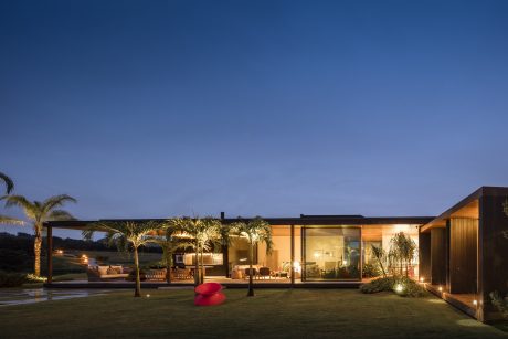 Modern open-concept home with expansive glass walls, lush landscaping, and cozy outdoor seating.