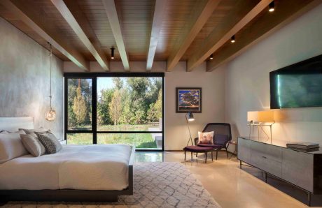 A spacious bedroom with a wooden beamed ceiling, large windows, and a modern interior design.