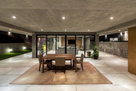 Sleek concrete ceiling, floor-to-ceiling glass walls, and a cozy dining area with a wooden table.