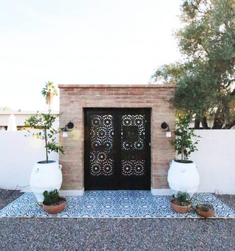 A charming, brick-framed entryway with ornate black metal doors and decorative planters.