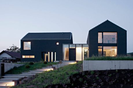 Striking modern home with sleek black exterior, large windows, and well-lit interior spaces.