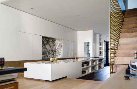 Sleek, modern kitchen with white cabinets, marble countertops, and wood accents. Geometric lighting and shelving add visual interest.