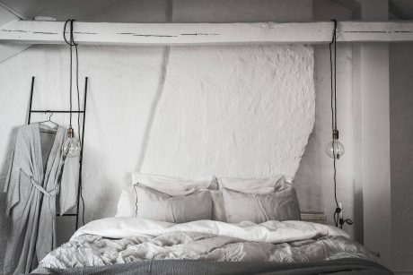 Minimalist bedroom interior with hanging lights, cozy bedding, and a neutral color palette.